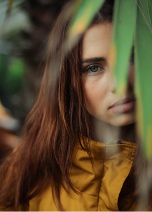 portrait photo of a young women will long hair partially behind the plants of an exotic plant