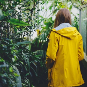 girll in a yellow coat seen from behind against a wall of greenery